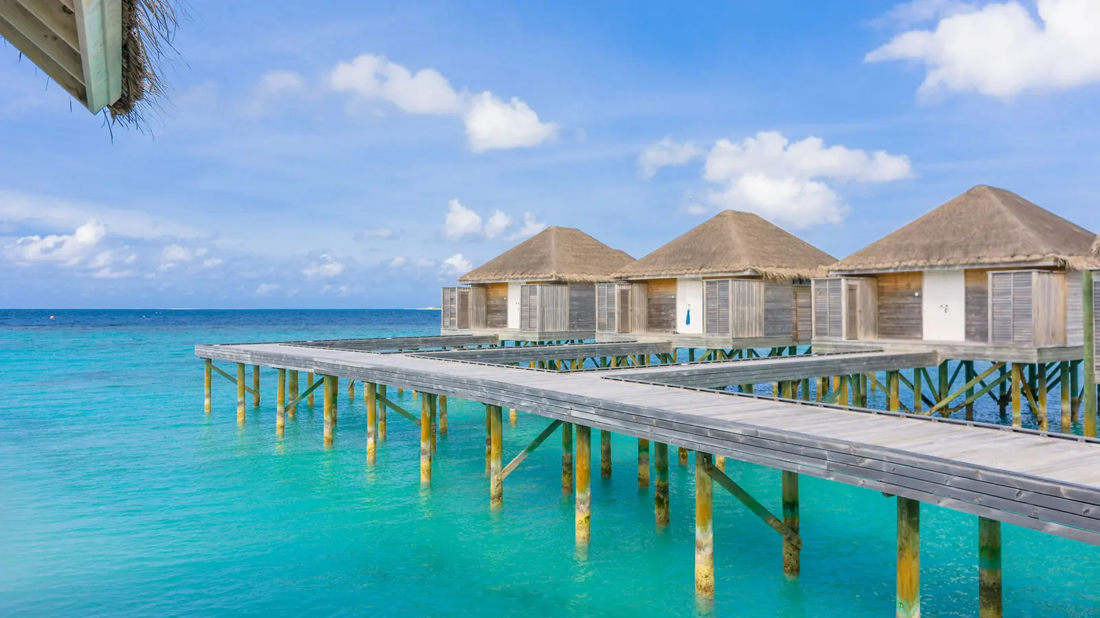 Thatched overwater villas along a wooden jetty above a turquoise lagoon in the Maldives