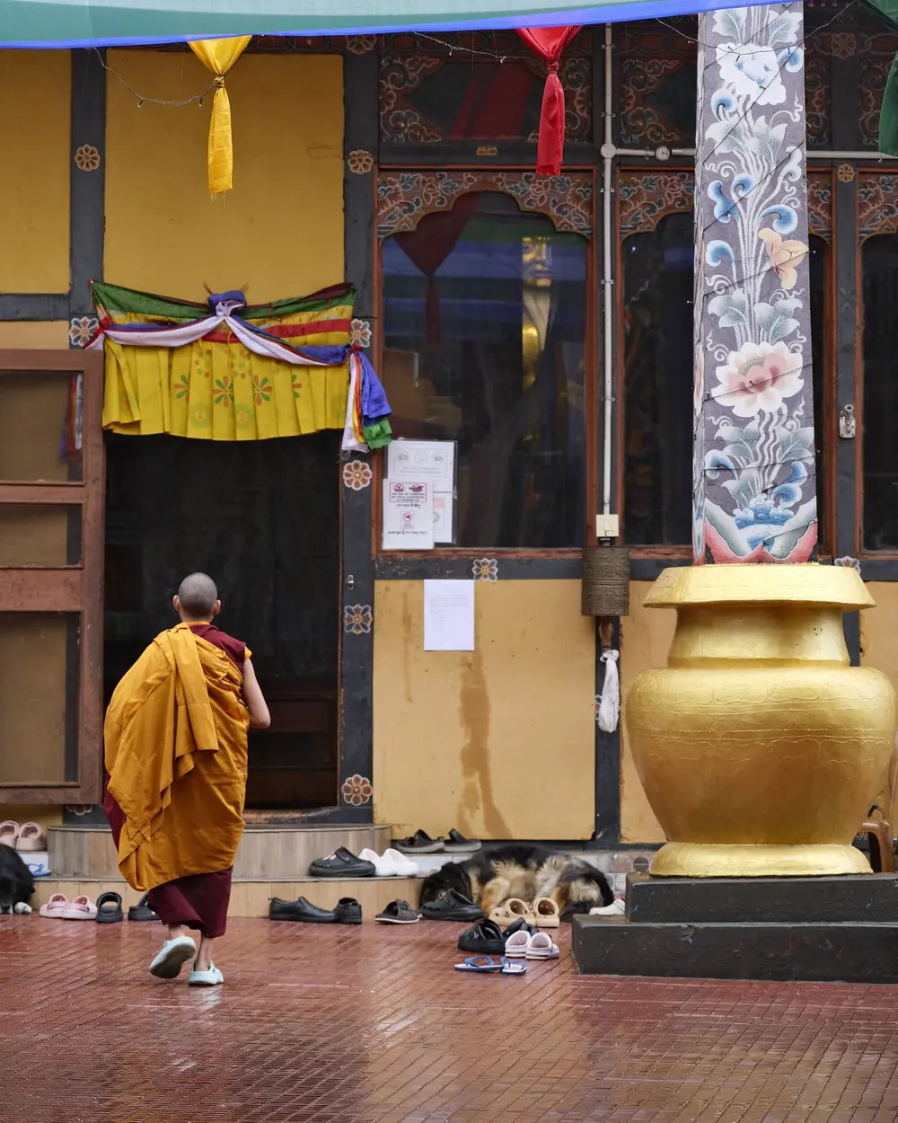 A Buddhist monk walks near a beautifully decorated temple entrance in Bhutan, showcasing cultural and spiritual symbolism