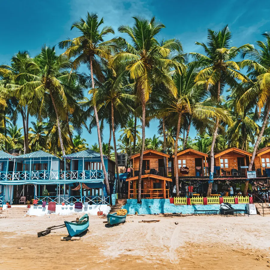 Colorful beach huts and palm trees on a sandy shore under a blue sky