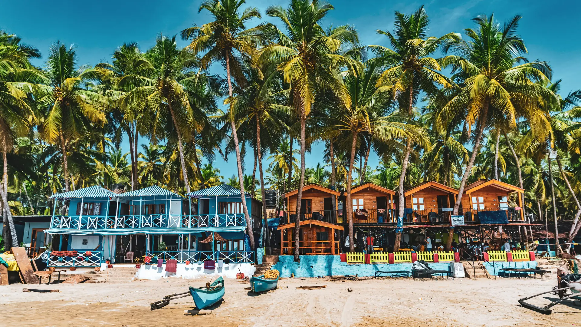 Colorful beach huts and palm trees on a sandy shore under a blue sky