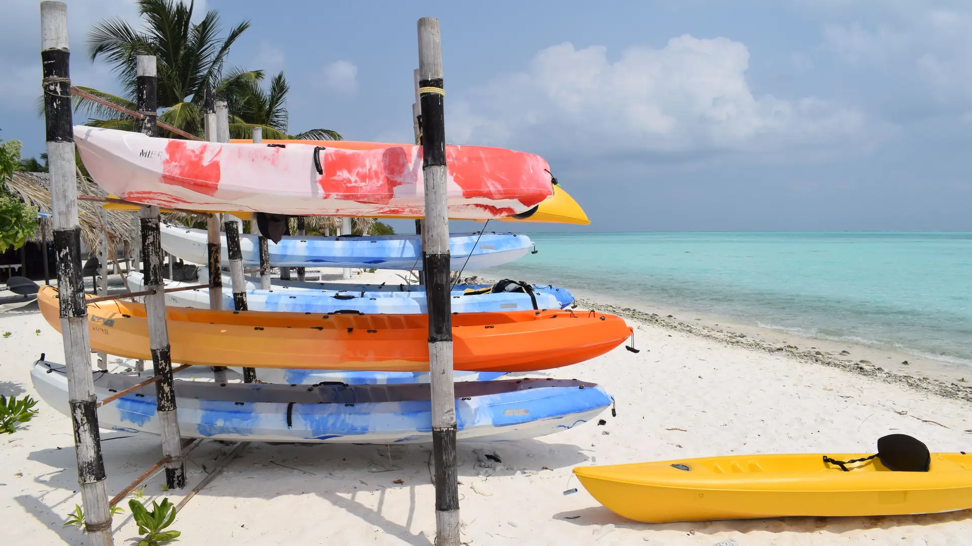 Colorful kayaks stacked on the sandy shores of Minicoy Island, India, with a clear turquoise sea backdrop