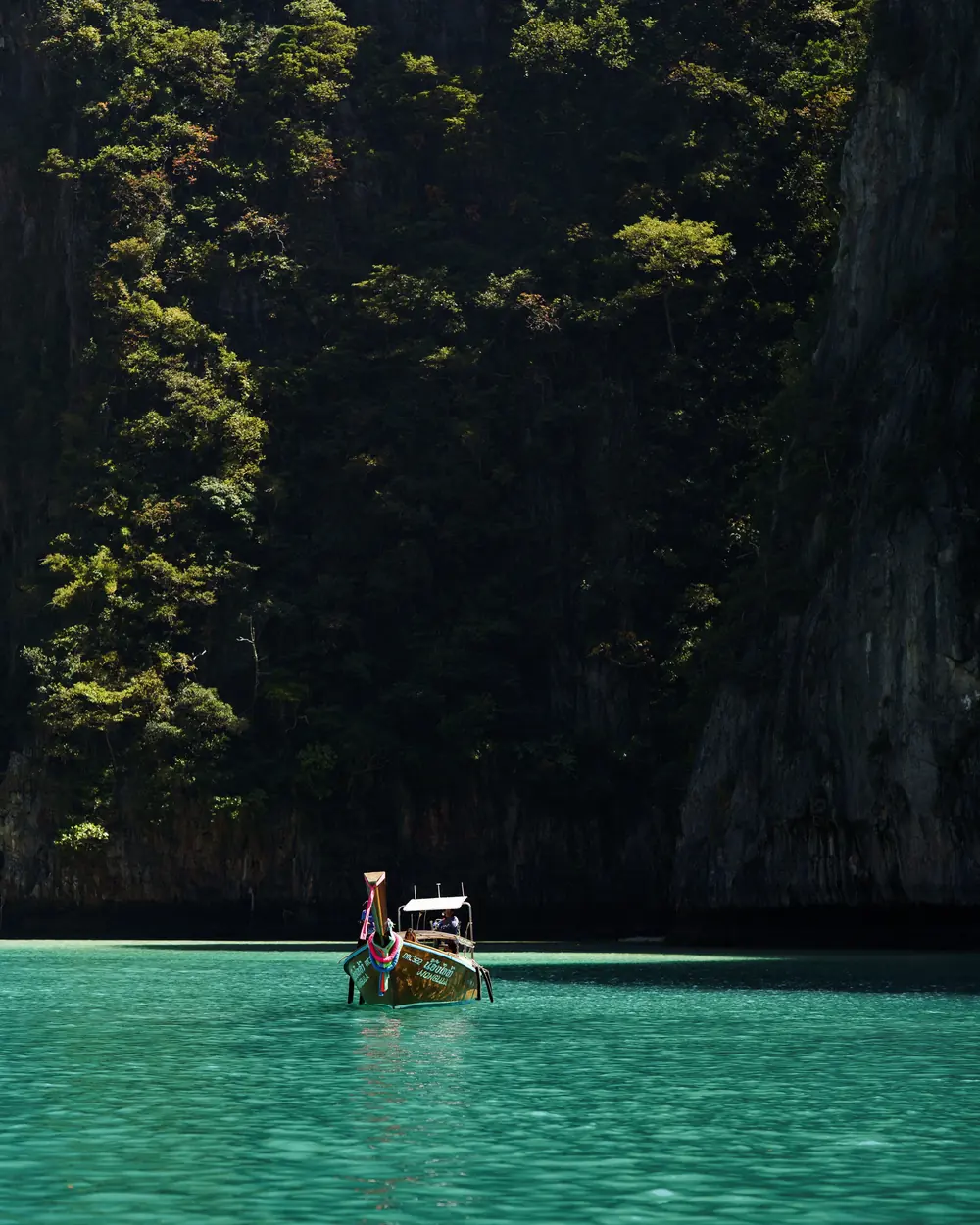 Longtail boat floats serenely in a Phi Phi Islands lagoon, surrounded by lush cliffs